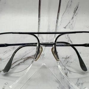 Könnte beinhalten: Schwarze Aviator-Sonnenbrille mit silbernem Metallrahmen. Der Rahmen trägt den Text "Securitas" auf der linken Seite und "Riccardo Frame Italy" auf der rechten Seite.