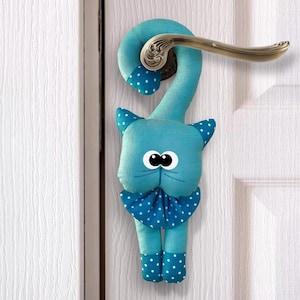 Może przedstawiać: Niebieski, kotwiowy kształt drzwi z białymi kropkami i dużymi czarnymi oczami. Kot trzyma klamkę.