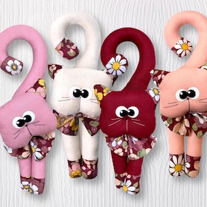 May include: Four plush cat toys with long tails, each in a different color: pink, white, burgundy, and peach. Each cat has a floral pattern on its body and a bow around its neck. The cats have large, black eyes and a black nose.