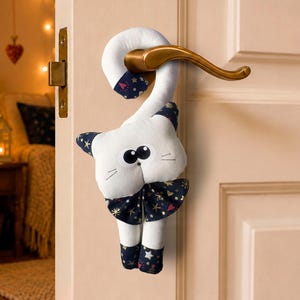 May include: A white fabric cat door hanger with a long curved tail that hooks over a door handle. The cat features large black and white eyes, embroidered whiskers, and a dark blue bow tie and paw accents decorated with a pattern of stars and hearts.