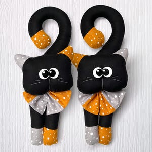 May include: Two black fabric cat doorstops with orange and white polka dot bows. The cats have black eyes and white whiskers.