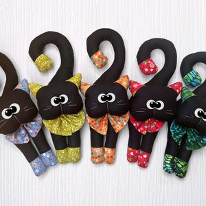 May include: Five black fabric cat toys with different colored bows and patterns. The cats are all curled up in a circle.