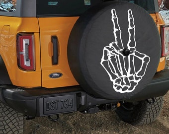 May include: A yellow Ford Bronco with a black spare tire cover featuring a white skeleton hand making a peace sign. The license plate reads "DST 734".
