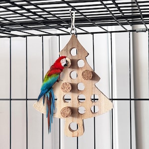 May include: A wooden bird toy shaped like a Christmas tree with cork rings hanging from it. A red and blue macaw is perched on the toy.