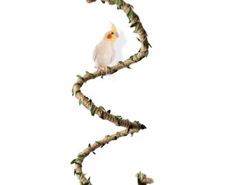 May include: A brown rope bird perch with green leaves wrapped around it. A small white bird with yellow and orange markings is perched on the rope.
