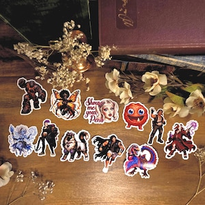 May include: A collection of eleven assorted stickers featuring fantasy characters, a creature, a dog, and a sticker with the text Show me your PENIS. The designs include a rock monster, a fairy, a warrior, a wizard, and a colourful feathered dinosaur.