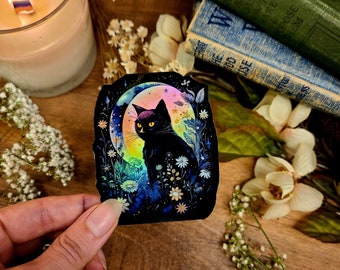 May include: A black cat with yellow eyes sits in a field of flowers under a crescent moon. The moon is iridescent and the flowers are a variety of colors. The background is dark blue with stars.