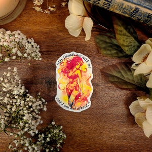 May include: A sticker featuring a woman with red hair and a fiery orange and yellow aura. The text on the sticker reads "My friends are with me and I am not afraid."