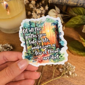 May include: A colorful sticker with the text "Of all the paths you take in life, make sure a few of them are dirt." The sticker features a forest scene with a path and sunlight.