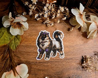 May include: A die-cut sticker featuring a long-haired cat with black and brown fur, wearing a purple jewelled crown, a matching collar with a butterfly pendant, and ornate purple gemstone cuffs on its front legs, with a white lacy pattern on its back.