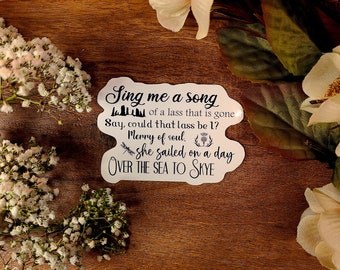 May include: White sticker with black text that reads "Sing me a song of a lass that is gone. Say, could that lass be 1? Merry of soul. She sailed on a day OVER THE SEA TO SKYE". The sticker has a small illustration of a dragonfly and a thistle.