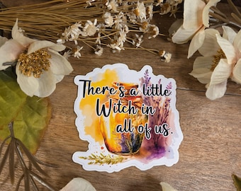 May include: A die-cut sticker featuring a watercolor illustration of a glass jar filled with golden liquid and dried herbs. The text "There's a little Witch in all of us." is printed in black over the jar, surrounded by yellow and purple paint splashes.
