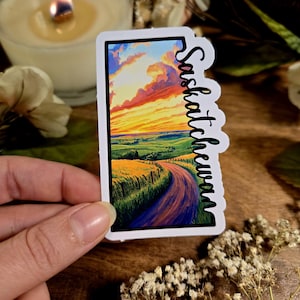 May include: A sticker featuring a scenic landscape of a winding road through a field with a sunset sky. The text "Saskatchewan" is written vertically on the right side of the sticker.