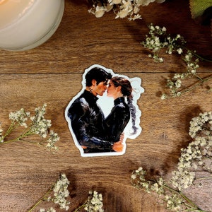 May include: A sticker featuring a romantic illustration of a couple in black clothing, embracing and looking at each other with affection.