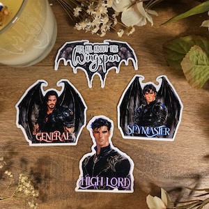 Może przedstawiać: Cztery naklejki z postaciami z powieści fantasy. Naklejki są białe z czarnymi obramowaniami i przedstawiają ilustracje mężczyzn z skrzydłami. Tekst na naklejkach brzmi "It's all about the Wingspan", "General", "Spymaster" i "High Lord".