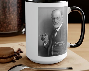 May include: White ceramic mug with a black rim and handle. The mug features a black and white photo of Sigmund Freud with a cigarette in his hand. The text "That's what your mom said" is printed below the photo.