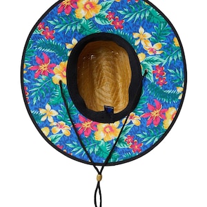 May include: A straw sun hat with a vibrant floral pattern. The hat features a wide brim with a blue background adorned with colorful flowers and green leaves. It has a black trim and a chin strap with a wooden bead.