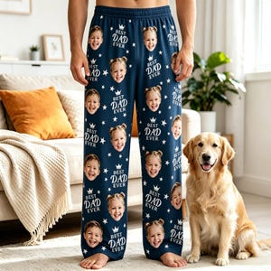 May include: Navy blue pajama pants featuring a repeating pattern of white stars, crowns, and the text "BEST DAD EVER" interspersed with photographic portraits of a child's face. The pants have an elastic waistband and a relaxed fit.