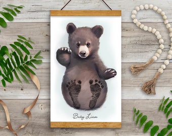 May include: A framed print of a brown bear cub with its paws imprinted in black paint. The print has a white background and the text "Baby Liam" is written at the bottom.