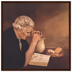 Op de afbeelding: Een vrouw met wit haar bidt met haar handen gevouwen. Ze draagt een zwarte jurk en zit aan een tafel met een boek, een kan en brood. Het boek is open en er liggen brillen op.