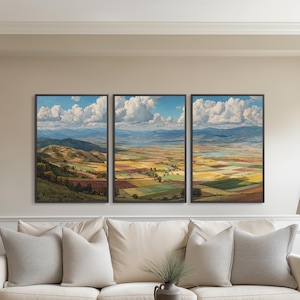 May include: A triptych of framed landscape paintings depicting a colorful valley under a blue sky with fluffy white clouds. The artwork is displayed above a cream-colored sofa with gray pillows, a wooden coffee table, and two matching lamps.