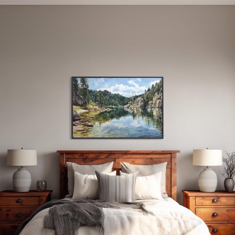 May include: A framed landscape painting depicts a serene lake scene with reflections of trees and rocks. The artwork, with a black frame, hangs above a wooden bed frame, complemented by matching nightstands and lamps.