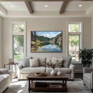 May include: A living room with a large landscape painting above a beige sofa. The painting depicts a serene lake scene with mountains and trees. The room has large windows, a coffee table, and decorative pillows.