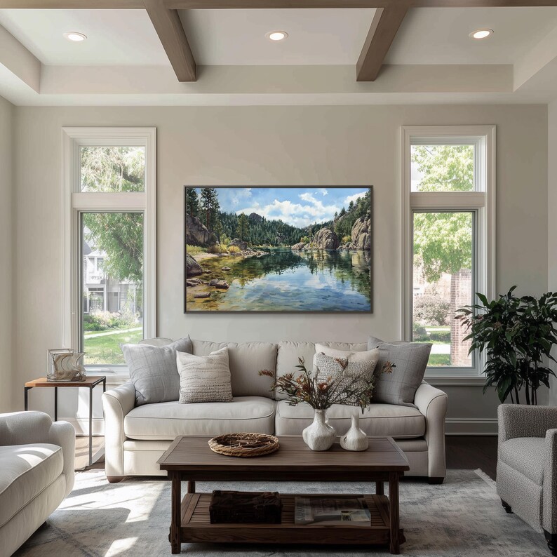 May include: A living room with a large landscape painting above a beige sofa. The painting depicts a serene lake scene with mountains and trees. The room has large windows, a coffee table, and decorative pillows.