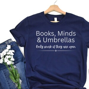 May include: A navy blue t-shirt with white text that reads "Books, Minds & Umbrellas Only work if they are open".
