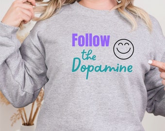 May include: A gray sweatshirt with the text "Follow the Dopamine" in purple and teal lettering, and a black smiley face.