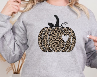 May include: A gray sweatshirt with a black and brown leopard print pumpkin with a white heart in the center. The pumpkin has a black stem and green leaves.