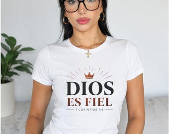 May include: A white short-sleeved t-shirt featuring a graphic print with a brown crown icon above the text DIOS ES FIEL and the reference 1 CORINTIOS 1:9 in black and brown lettering centered on the chest area of the garment.