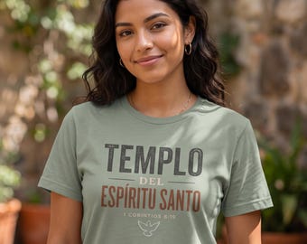 May include: A sage green short-sleeved t-shirt featuring the text TEMPLO DEL ESPÍRITU SANTO in dark gray and brown lettering, with the reference 1 CORINTIOS 6:19 and a small white outline of a dove centered below the text.