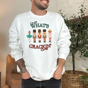 May include: White sweatshirt with a graphic of a ballerina and nutcracker soldiers. The text "What's Crackin'" is printed below the graphic.