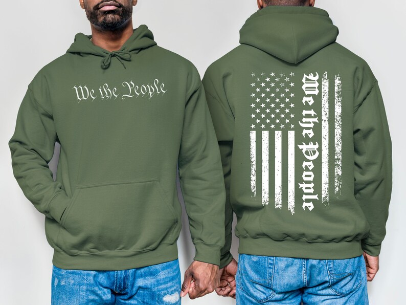 K&ouml;nnte beinhalten: Ein gr&uuml;ner Kapuzenpullover mit dem Aufdruck "We the People" auf der Vorderseite und einem abgenutzten amerikanischen Flaggenmuster auf der R&uuml;ckseite.