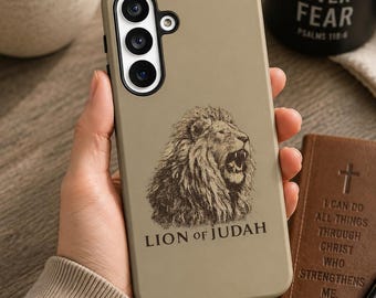 May include: A tan smartphone case featuring a detailed black line-art illustration of a roaring lion. Below the lion, the text reads "LION of JUDAH" in a serif font. The case has a cutout for a triple-lens camera system on the upper left side.