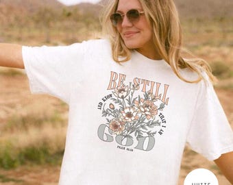 May include: White t-shirt with a floral design and the text "Be Still and Know That I Am God" with the scripture reference "Psalm 46:10".