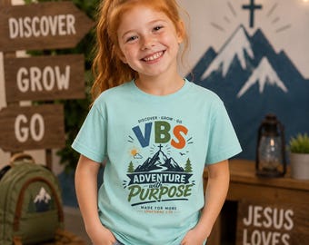 May include: A light blue short-sleeve t-shirt featuring a graphic print with the text VBS ADVENTURE WITH PURPOSE, DISCOVER GROW GO, and MADE FOR MORE EPHESIANS 2:10, accompanied by illustrations of a mountain, trees, a sun, and a cross.