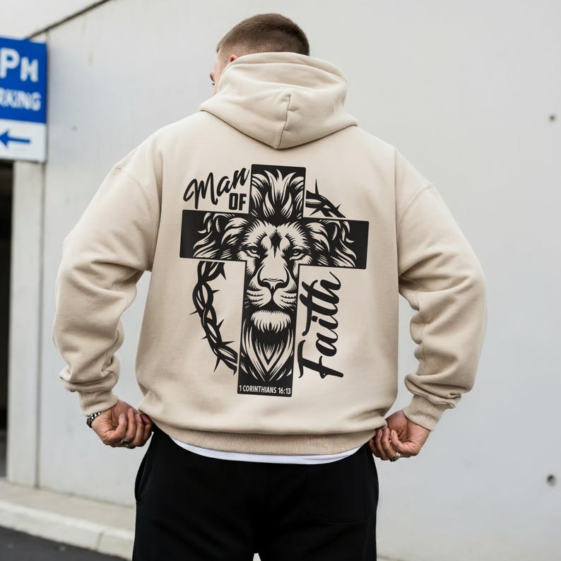 May include: Beige hoodie with a large graphic on the back. The graphic features a lion's face within a cross, with the words "Man of Faith" and a Bible verse. The hoodie has a hood and long sleeves.