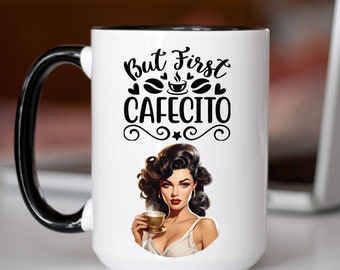 May include: White ceramic coffee mug with a black handle and black rim. The mug has a black and white graphic of a woman with dark hair holding a coffee cup. The text on the mug reads "But First Cafecito".