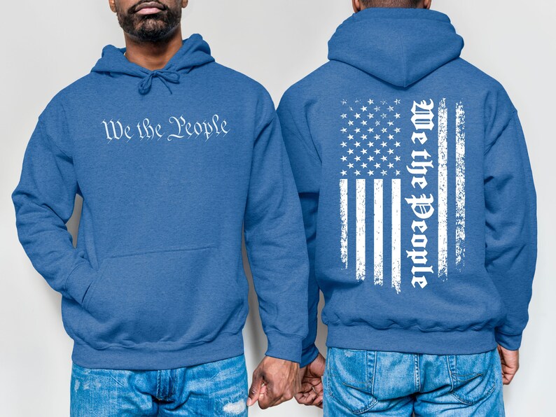 K&ouml;nnte beinhalten: Zwei blaue Kapuzenpullover mit dem Aufdruck "We the People". Ein Pullover hat den Aufdruck auf der Vorderseite, der andere eine abgenutzte amerikanische Flagge mit dem Aufdruck auf der R&uuml;ckseite.