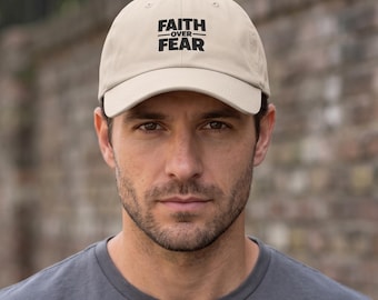 May include: A beige baseball cap featuring the black text FAITH OVER FEAR printed on the front panel. The cap has a structured crown, a curved brim, and a button on the top center. The design is centered on the front of the hat.