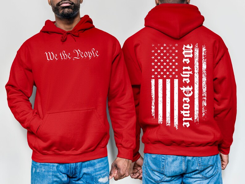 K&ouml;nnte beinhalten: Zwei rote Kapuzenpullover mit dem Aufdruck "We the People". Ein Pullover hat ein wei&szlig;es, abgenutztes amerikanisches Flaggenmuster auf der R&uuml;ckseite.