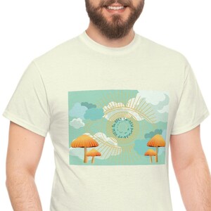 Könnte beinhalten: Ein weißes T-Shirt mit einem Aufdruck eines blauen und grünen Auges mit einem goldenen Ring darum. Das Auge ist von Wolken und Pilzen umgeben. Der Aufdruck ist mittig auf dem T-Shirt platziert.