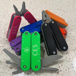 May include: A collection of multi-tools in various colors, including pink, blue, orange, purple, green, and black. Each tool features a different design, with some including pliers and blades. The text "CES" is printed on some of the tools.