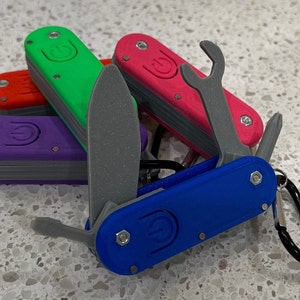 May include: A collection of multi-tools in various colors, including blue, green, red, pink, and purple. The tools feature a blade, screwdriver, wrench, and bottle opener. Each tool has a power button symbol and a metal carabiner clip.