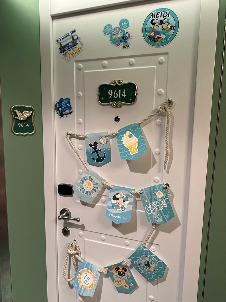 Puede incluir: Una puerta blanca con marco verde decorada con pegatinas de tem&aacute;tica n&aacute;utica y una cuerda de banderas. La puerta tiene una placa de n&uacute;mero con el n&uacute;mero 9614. Las banderas tienen im&aacute;genes de Mickey Mouse, un ancla de barco y helado.
