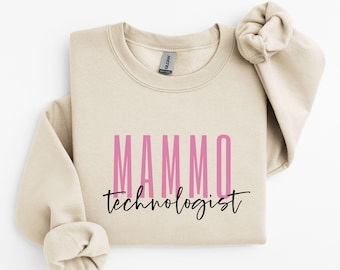 Puede incluir: Una sudadera de color beige con el texto "MAMMO technologist" impreso en ella. La palabra "MAMMO" está en letras rosas y la palabra "technologist" está en letras negras.