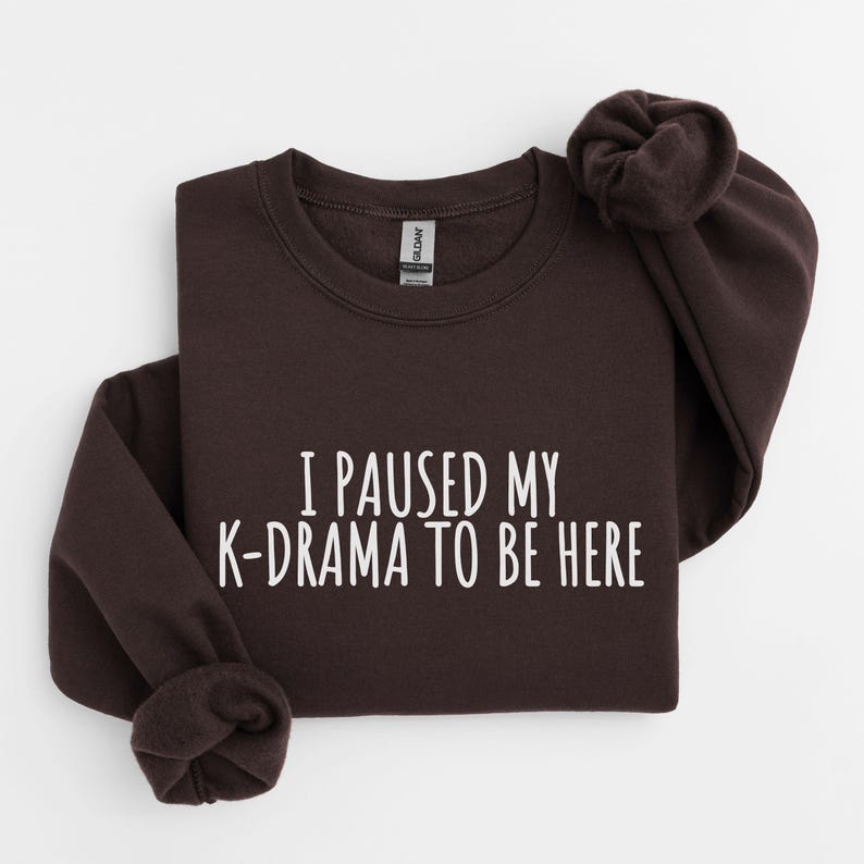 May include: A dark brown sweatshirt with the text "I paused my K-drama to be here" printed in white.