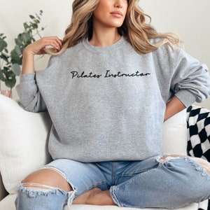 May include: A gray sweatshirt with the text "Pilates Instructor" in black lettering.